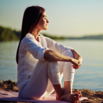 Brunette woman sitting on a yoga mat at the seaside