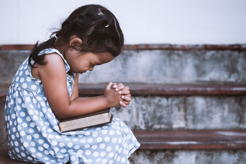 Little girl in blue polka dot dress and a Bible prays